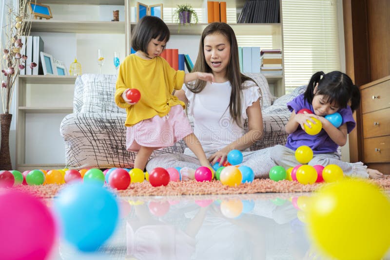 Ein asiatisches Geschwister und eine jüngere Schwester spielen in ihrem Wohnzimmer mit bunten Bällen lizenzfreies stockbild