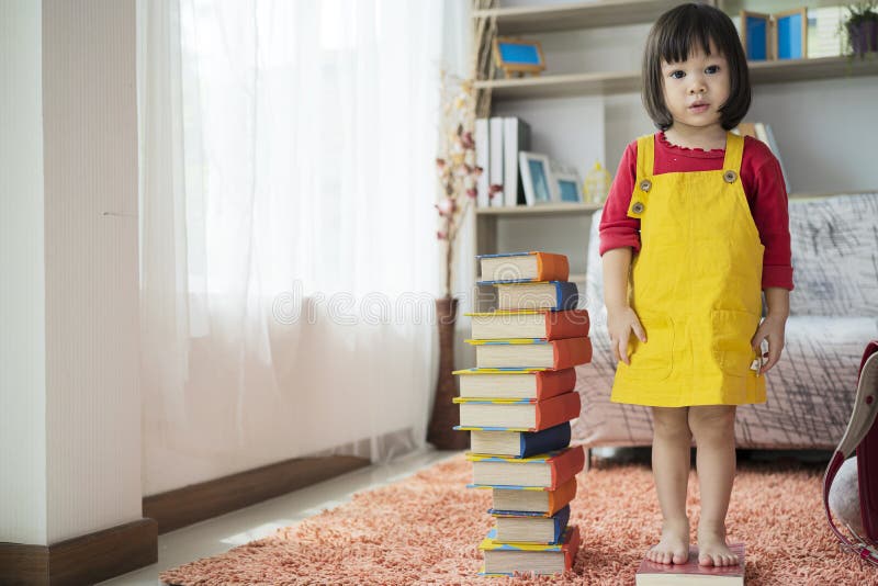 Ein asiatisches Mädchen, das im Kindergarten studiert, steht auf einem Buch mit einer Höhe stockbild