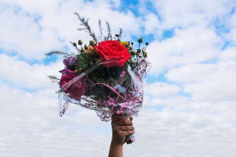 a bouquet of flowers in hand on blue sky background. hand of the child holds a gift a bouquet of beautiful flowers on September 1. a bouquet of flowers in hand on blue sky background. hand of the child holds a gift a bouquet of beautiful flowers on September 1.