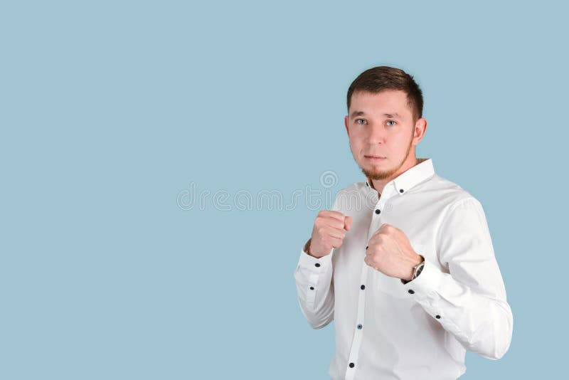 Ein bärtiger Mann in einem weißen Hemd demonstriert Stärke, indem er seine Hände in einer Faust vor seinem Copyspace festhält stockbilder