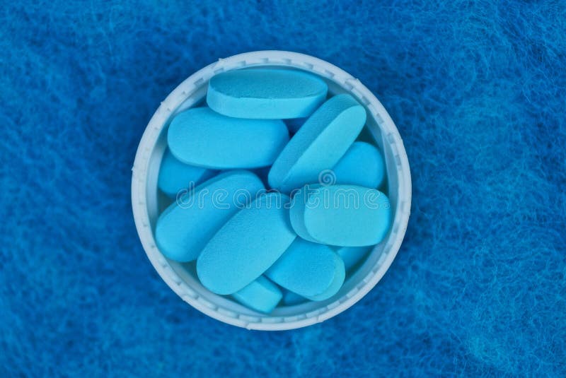 Ein Bündel blaue Pillen in einer weißen Flaschenkapsel auf einem woolen Stoff stockbild Ein Bündel blaue Pillen in einer weißen Flaschenkapsel auf einem woolen Stoff stockbild