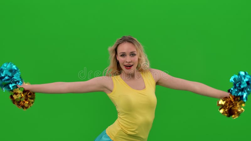Ein cheerleader tanzt einen feurigen cheerleader-tanz mit pompoms im studio auf einer grünen leinwand. das Mädchen bewegt ihre Hüf stock footage