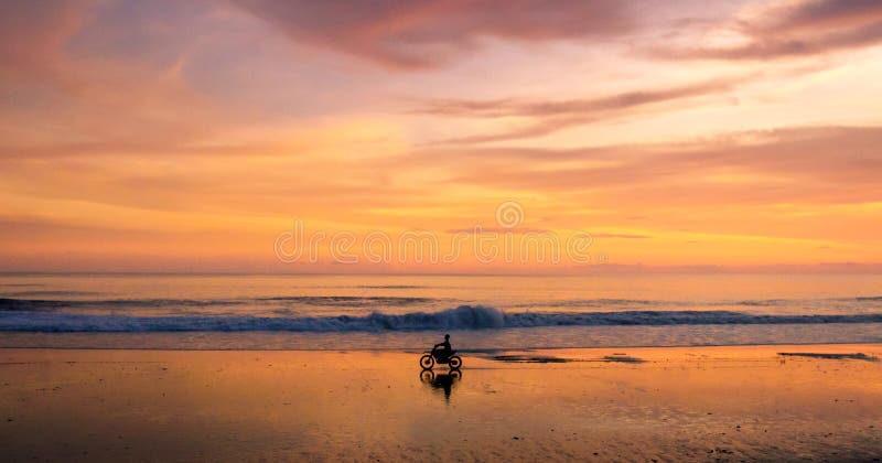 Ein einziges Motorrad und ein Reiter, die entlang einen Strand bei Sonnenuntergang fahren stockbilder Ein einziges Motorrad und ein Reiter, die entlang einen Strand bei Sonnenuntergang fahren stockbilder