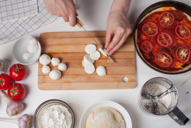 Ein Frauenchef schneidet Mozzarellakäse, um eine italienische selbst gemachte Pizza zu machen Auf der weißen Tabelle sind Mozzare lizenzfreie stockbilder Ein Frauenchef schneidet Mozzarellakäse, um eine italienische selbst gemachte Pizza zu machen Auf der weißen Tabelle sind Mozzare lizenzfreie stockbilder