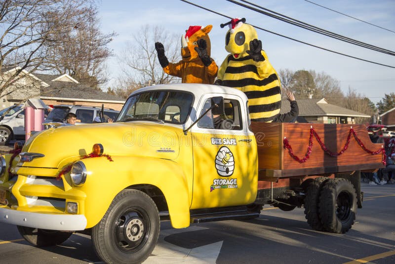 Ein gelber Lastwagen, der in einer Parade mit zwei in Kostümen gekleideten Personen fährt