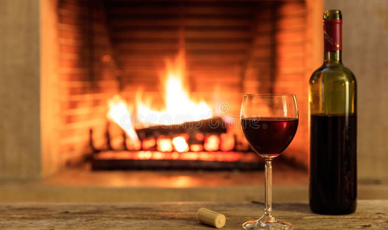Ein Glas und eine Flasche Rotwein auf brennendem Kaminhintergrund stockbilder Ein Glas und eine Flasche Rotwein auf brennendem Kaminhintergrund stockbilder