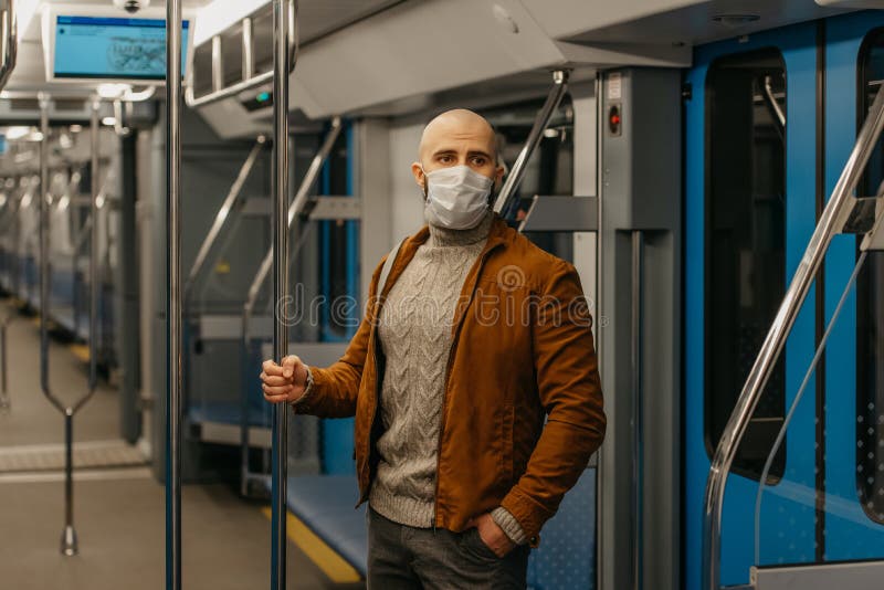 Ein glatzköpfiger Mann mit einem Bart in einer Gesichtsmaske hält das Geländer in einem U-Bahn-Auto. Ein Mann mit einem Bart in einer medizinischen Gesichtsmaske, um die Ausbreitung von covid19 zu vermeiden, fährt mit der U-Bahn und hält das Geländer. ein kahler Kerl in einer chirurgischen Maske hält soziale Distanz im Zug