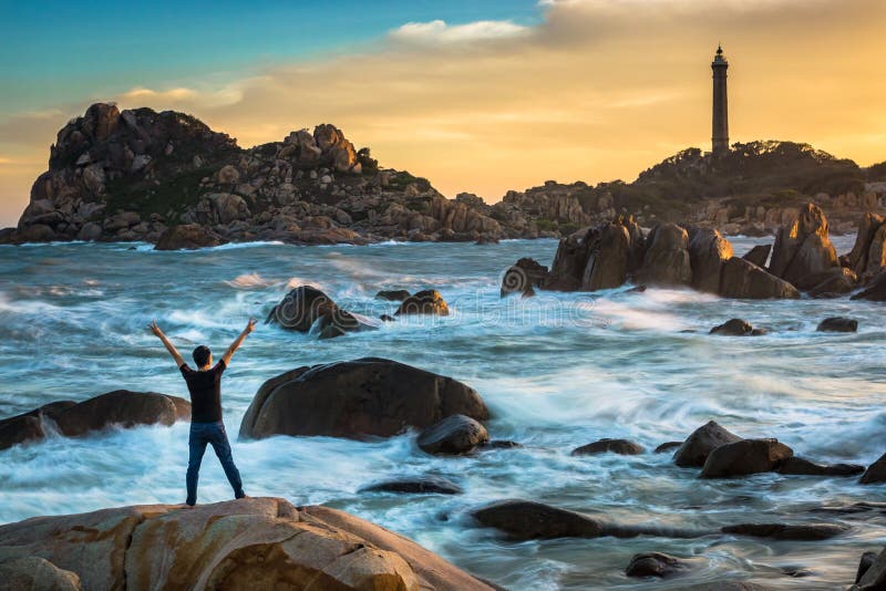Ein glücklicher Mann, der Sieg auf die Oberseite eines großen Felsens durch den Ozean feiert stockfotos Ein glücklicher Mann, der Sieg auf die Oberseite eines großen Felsens durch den Ozean feiert stockfotos