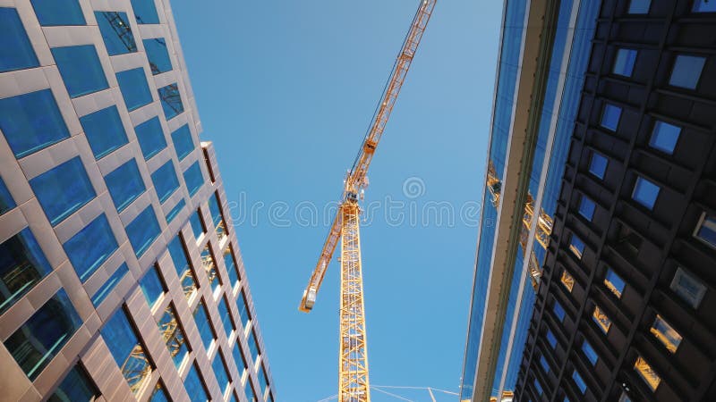 Ein großer Turmkran im Stadtzentrum der modernen Stadt Glasbürogebäude herum Breiter Schuss des niedrigen Winkels stockbild Ein großer Turmkran im Stadtzentrum der modernen Stadt Glasbürogebäude herum Breiter Schuss des niedrigen Winkels stockbild