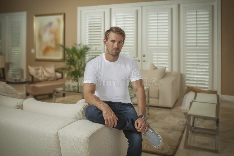 Ein gut aussehender Mann stellt auf den Arm der Couch kreuzte Beinblicke an der Kamera ein lizenzfreie stockfotografie Ein gut aussehender Mann stellt auf den Arm der Couch kreuzte Beinblicke an der Kamera ein lizenzfreie stockfotografie