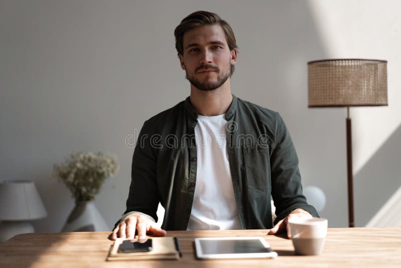 Ein guter Mitarbeiter des Jahrtausendbüros sitzt am Schreibtisch und lächelt sich die Kamera an lizenzfreies stockfoto