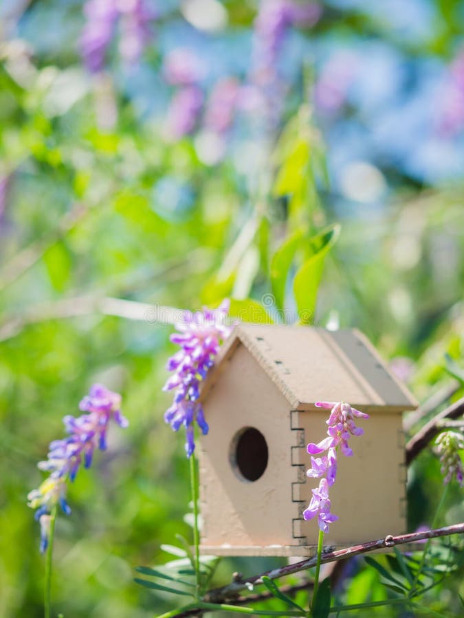 Ein hölzernes Spielzeugvogelhaus in den freundlichen violetten Strich blauen Blumen stockbild