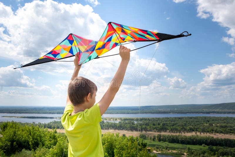 Ein Junge mit einem bunten Drachen in seinen Händen gegen den blauen Himmel mit Wolken Ein Kind in einem gelben T-Shirt und in de stockbild Ein Junge mit einem bunten Drachen in seinen Händen gegen den blauen Himmel mit Wolken Ein Kind in einem gelben T-Shirt und in de stockbild