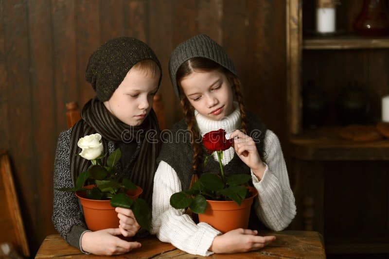 Ein Junge mit einem Mädchen in einem Weinlesekleid, das an einem alten Schreibtisch sitzt Betrachten der Blumen lizenzfreie stockbilder Ein Junge mit einem Mädchen in einem Weinlesekleid, das an einem alten Schreibtisch sitzt Betrachten der Blumen lizenzfreie stockbilder