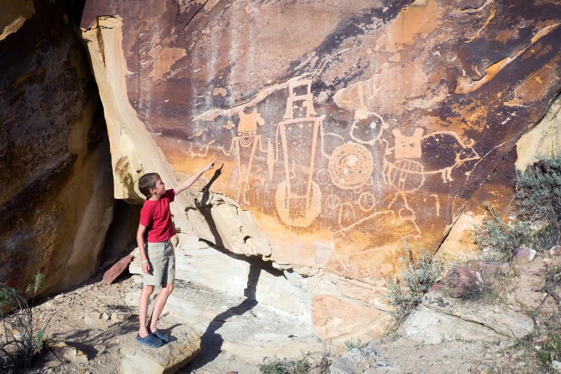 Ein Junge zeigt seine Hand auf der Wand mit Petroglyphen Dinosaurier Nati lizenzfreie stockbilder