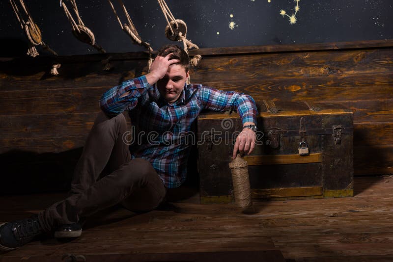 Ein junger enttäuschter Mann sitzt nahe einem Kasten und hält Glasflasche lizenzfreies stockfoto Ein junger enttäuschter Mann sitzt nahe einem Kasten und hält Glasflasche lizenzfreies stockfoto