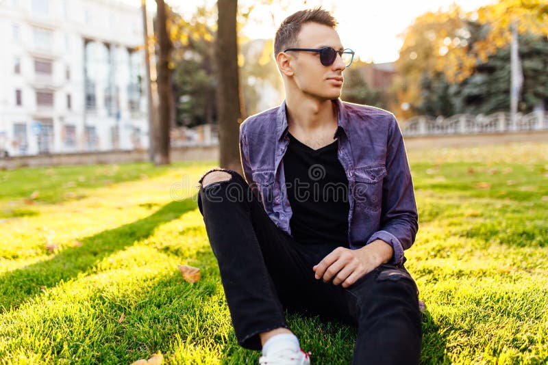 Ein junger Mann, gekleidet in der zufälligen Kleidung, sitzt in einem Park auf dem La stockfotografie Ein junger Mann, gekleidet in der zufälligen Kleidung, sitzt in einem Park auf dem La stockfotografie