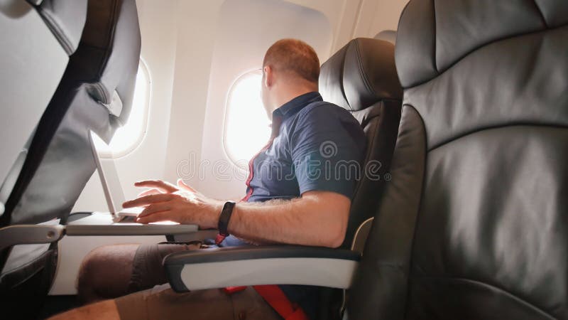 Ein junger Mann saß im Flugzeug und arbeitete an seinem Laptop vor Abfahrt