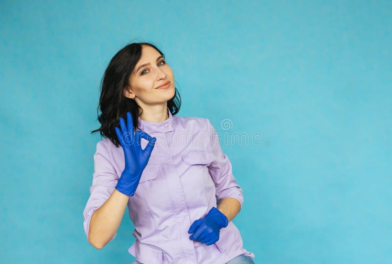 Ein junges Mädchen in den blauen medizinischen Handschuhen. die Krankenschwester oder die Doktorgesten mit dem okaysymbol. ein Mäd stockbild