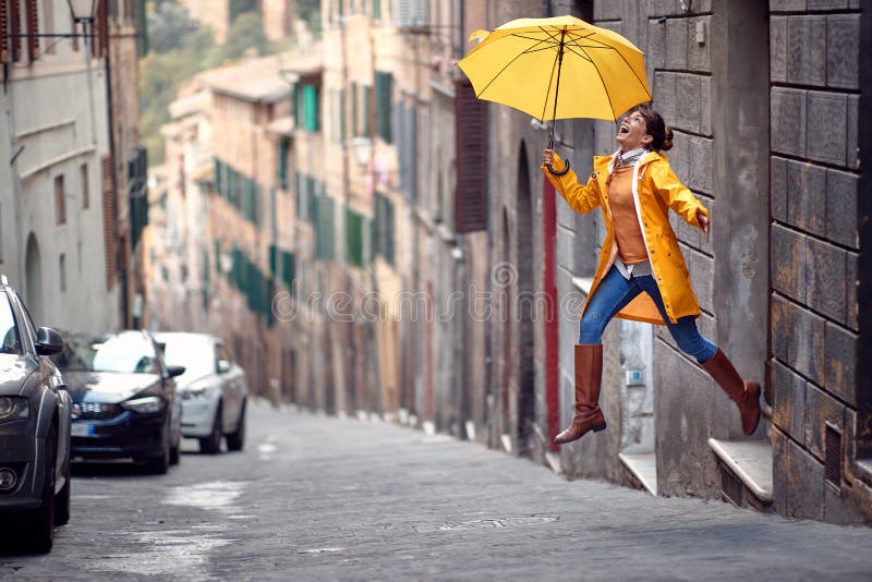 Ein junges Mädchen mit gelbem Regenmantel und Regenschirm springt auf die Straße, während es an einem regnerischen Tag durch die S
