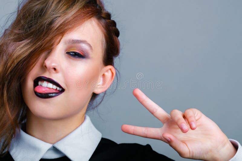 Ein junges Mädchen mit hellen Make-eup zeigt ein Siegeszeichen stockfoto