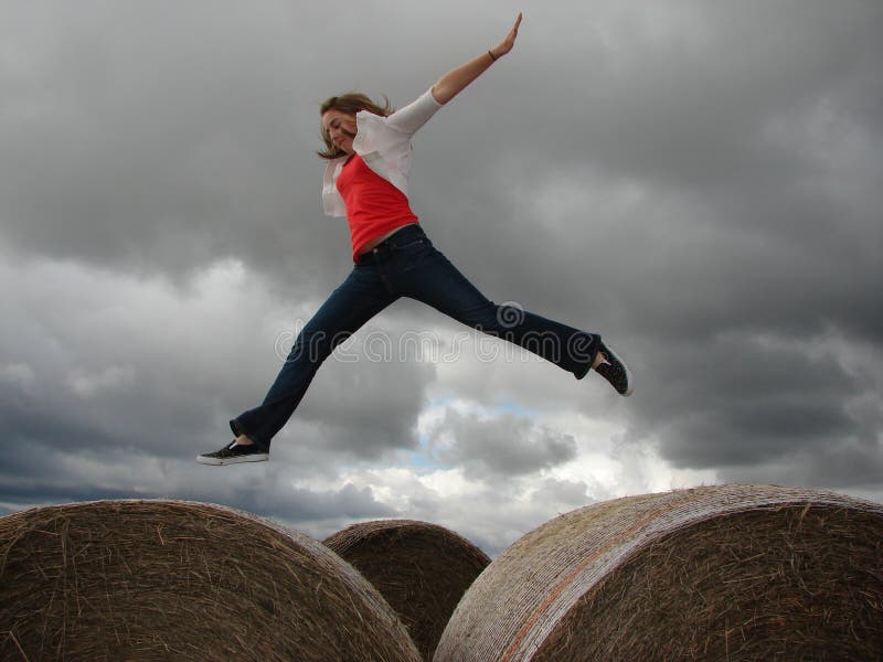 Ein junges Mädchen springt von einem Heuballen zu anderen an einem bewölkten Tag stockfoto Ein junges Mädchen springt von einem Heuballen zu anderen an einem bewölkten Tag stockfoto
