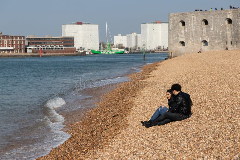 Ein junges Paar sitzt auf einem Kiesstrand und beobachtet die Wellen stockfoto Ein junges Paar sitzt auf einem Kiesstrand und beobachtet die Wellen stockfoto