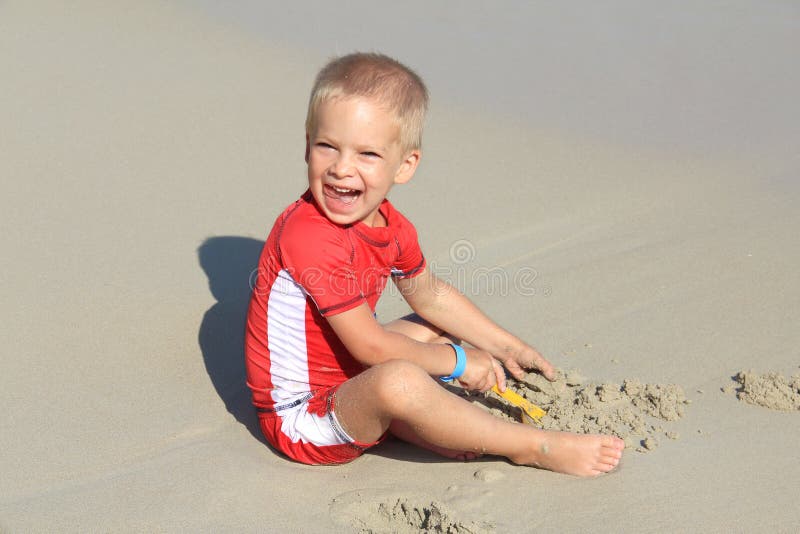 Ein kleiner blonder Junge in der Kleidung mit UV-Filter spielt mit Sand auf dem Strand durch das Meer, Feiertag mit den Kindern u stockbilder Ein kleiner blonder Junge in der Kleidung mit UV-Filter spielt mit Sand auf dem Strand durch das Meer, Feiertag mit den Kindern u stockbilder