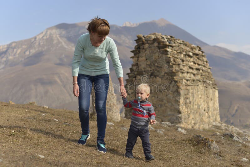 Ein kleiner Junge mit einem Friedensstifter reist mit seiner Mutter und geht unter den alten ossetischen Gebäuden stockfoto Ein kleiner Junge mit einem Friedensstifter reist mit seiner Mutter und geht unter den alten ossetischen Gebäuden stockfoto