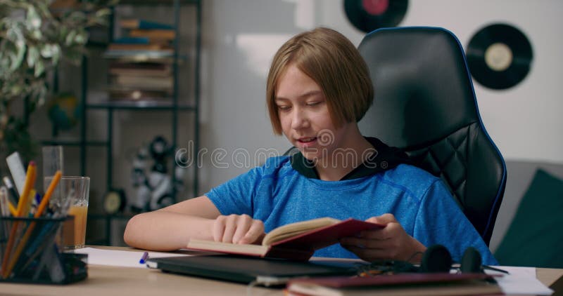 Ein kleiner Junge sitzt am Schreibtisch und liest sein Lieblingsbuch. das Kind die Seiten lacht und interessiert sich für