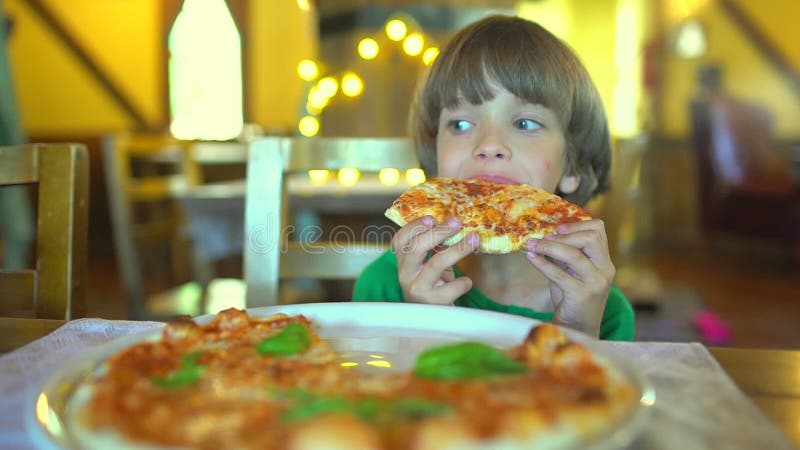 Ein kleines Kind in einem Schnellimbisscafé isst Pizza Porträt des netten lustigen kleinen kaukasischen Kinderjungen, der köstlic