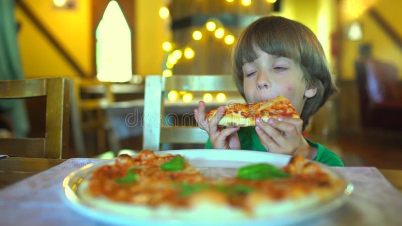 Ein kleines Kind in einem Schnellimbisscafé isst Pizza Porträt des netten lustigen kleinen kaukasischen Kinderjungen, der köstlic