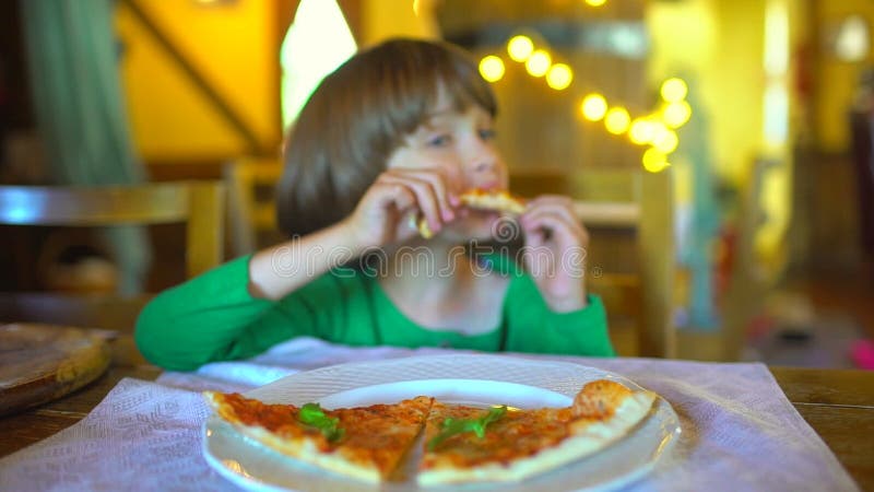 Ein kleines Kind in einem Schnellimbisscafé isst Pizza Porträt des netten lustigen kleinen kaukasischen Kinderjungen, der köstlic