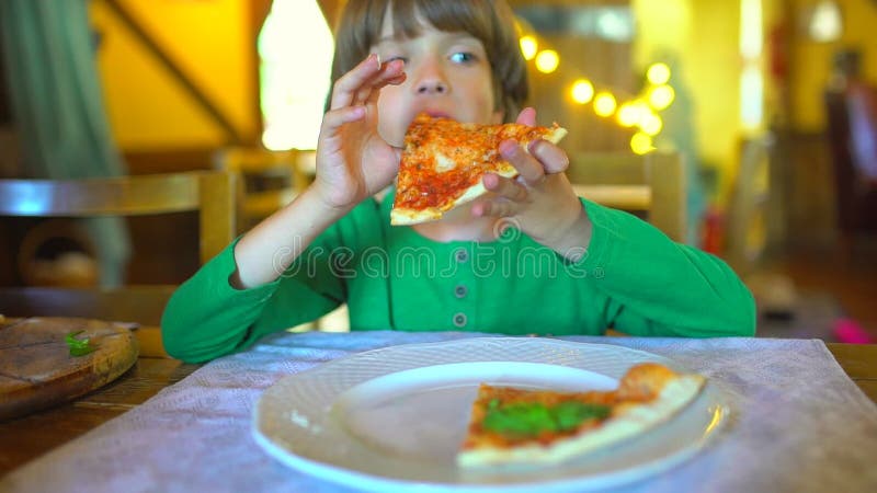 Ein kleines Kind in einem Schnellimbisscafé isst Pizza Porträt des netten lustigen kleinen kaukasischen Kinderjungen, der köstlic