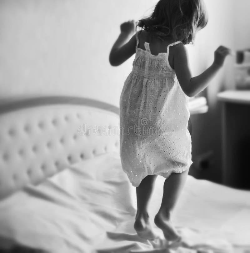 Ein kleines Mädchen, das auf ein Königgrößenbett springt lizenzfreies stockfoto Ein kleines Mädchen, das auf ein Königgrößenbett springt lizenzfreies stockfoto