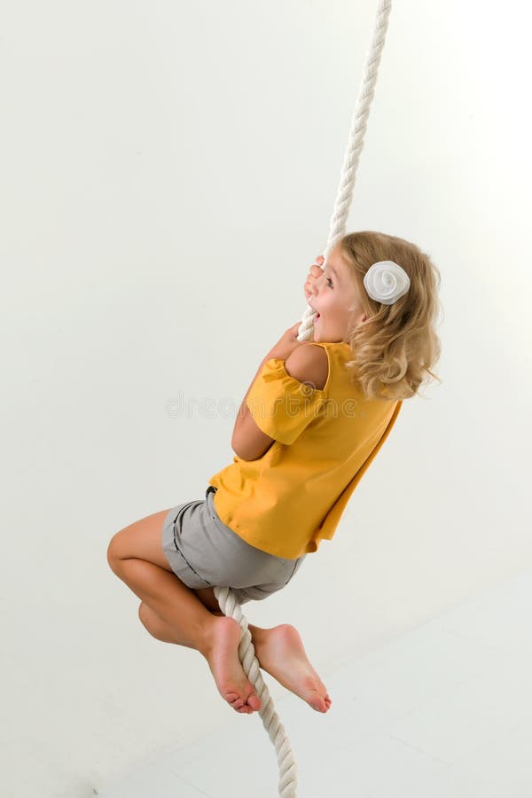 Ein kleines Mädchen hält an dem Seil mit ihren Händen, die auf ihm schwingen. lizenzfreies stockfoto