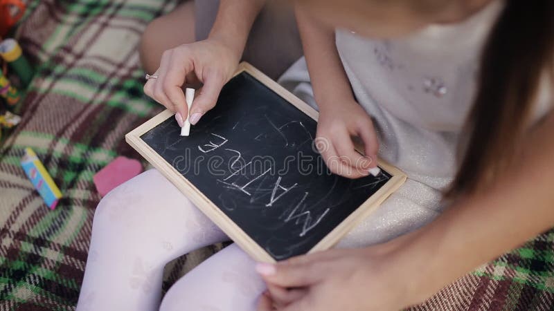 Ein kleines Mädchen lernt, Wörter auf die Tafel mit Kreide zu schreiben Mutter unterrichtet Tochter, Briefe, Alphabet zu schreibe