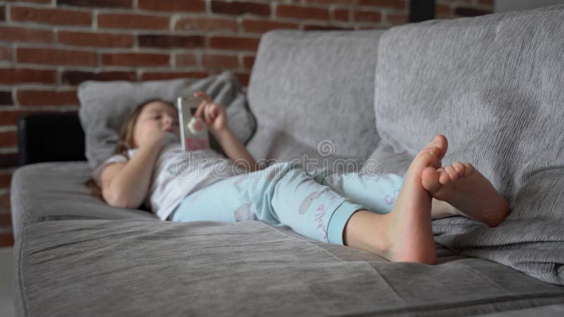 Ein Kleines Mädchen Liegt Zu Hause Auf Der Couch Und Schaut in Ein Smartphone. Das Kind Spielt Und Sieht Das Video Stock Footage - Video von lügen, leute: 215208316->