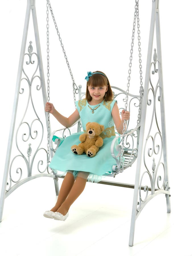 Ein kleines Mädchen schwingt auf einer Schaukel mit einem Teddybären. lizenzfreie stockbilder