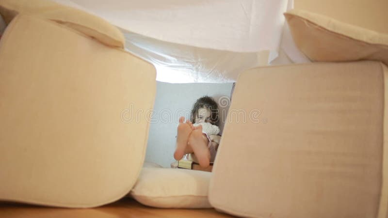Ein kleines Mädchen sitzt in einem behelfsmäßigen Haus von Kissen und von umfassenden Haus