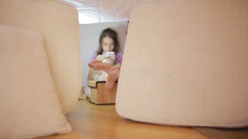 Ein kleines Mädchen sitzt in einem behelfsmäßigen Haus von Kissen und von umfassenden Haus