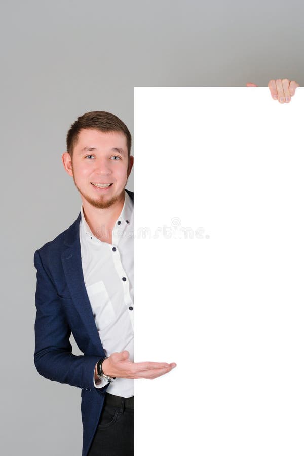 Ein lächelnder bärtiger Mann in seinen 30er-Punkten mit seiner Handfläche auf einer leeren weißen Tafel für Text und Werbetext lizenzfreies stockfoto