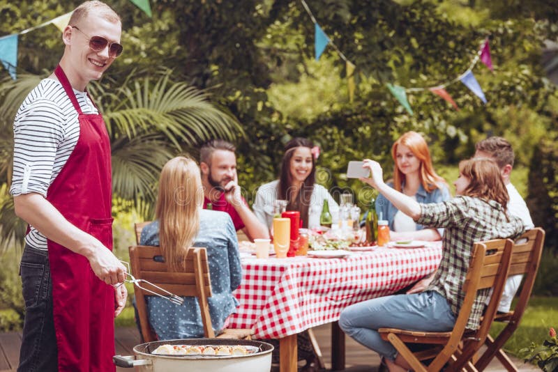 Ein lächelnder junger Mann, der ein Schutzblech grillt shashliks im f trägt lizenzfreie stockbilder Ein lächelnder junger Mann, der ein Schutzblech grillt shashliks im f trägt lizenzfreie stockbilder