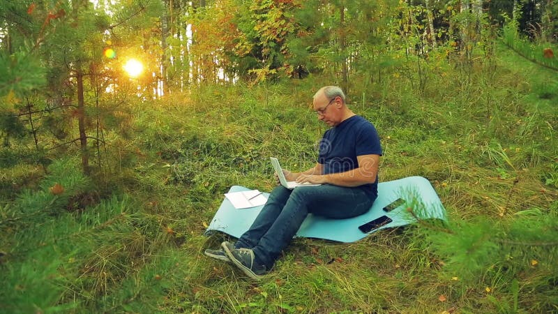 Ein Mann in den Gläsern auf einer Waldlichtung schreibt auf einer Laptoptastatur