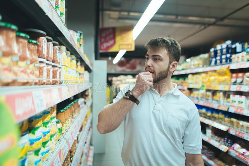 A man thinks what kind of product in a supermarket to choose. The buyer selects canned food at the store. Shopping in a supermarket. A man thinks what kind of product in a supermarket to choose. The buyer selects canned food at the store. Shopping in a supermarket.