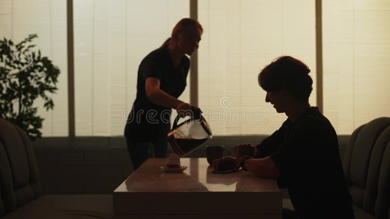 Ein Mann, der an der Fast-Food-Bar mit Smartphone-Kellnerin sitzt und mit Kaffeekanne Kaffee in seinem Schlamm gießt.