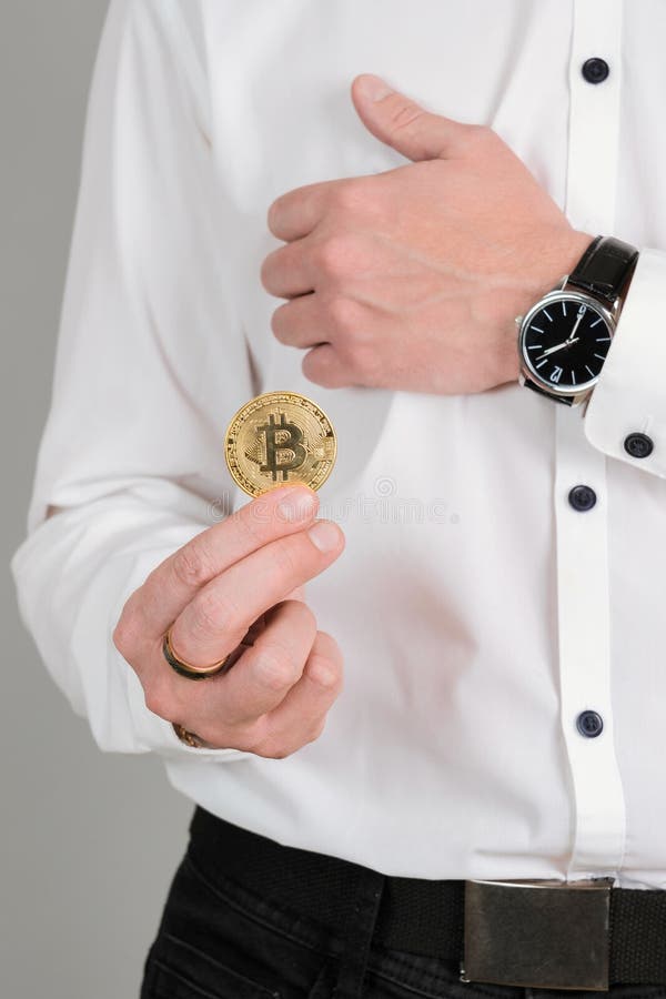 Ein Mann in einem weißen Hemd hält eine Goldmünze aus Bitcoin in seinem senkrechten Handfoto lizenzfreies stockfoto