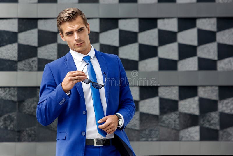 Ein Mann in einer blauen Klage gegen einen Hintergrund der dunklen modernen Architektur stockfotografie Ein Mann in einer blauen Klage gegen einen Hintergrund der dunklen modernen Architektur stockfotografie