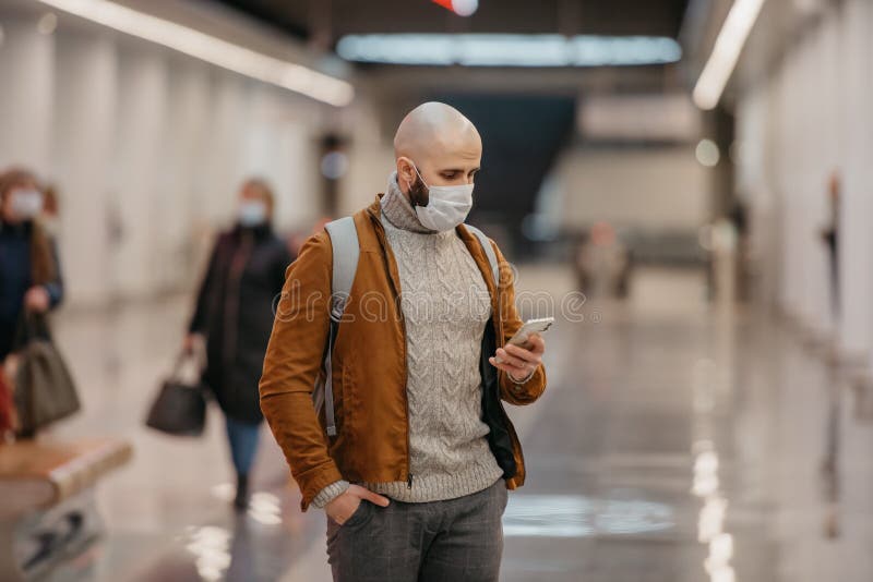 Ein Mann in einer Gesichtsmaske benutzt ein Smartphone, während er auf einen U-Bahn-Zug wartet lizenzfreies stockbild