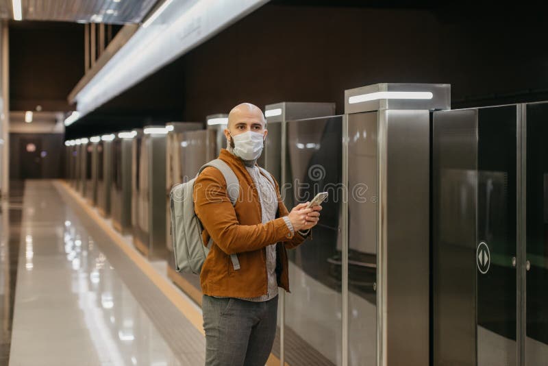 Ein Mann in einer Gesichtsmaske benutzt ein Smartphone, während er auf einen U-Bahn-Zug wartet lizenzfreies stockbild